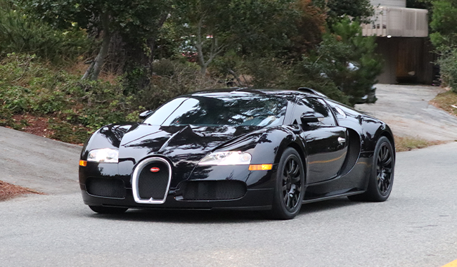 A black Bugatti Veyron pictured stationary on a road with a shrubbery behind - iconic cars