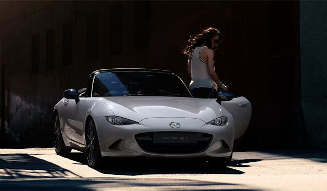 A silver Mazda MX-5 with a woman stood facing away in front of the driver's open door - Iconic cars