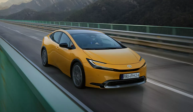 A yellow Toyota Prius pictured driving on a road with a mountain landscape - iconics