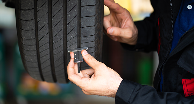 Tyre Wear and Wheel Imbalance: Mechanic checking checking the depth of car tyre tread. 