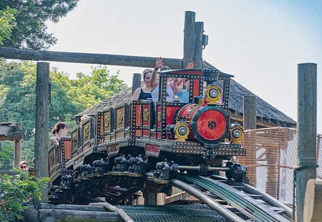 Thrill-seekers cheering on a vintage train-themed family rollercoaster at a Alton Towers during school holidays.