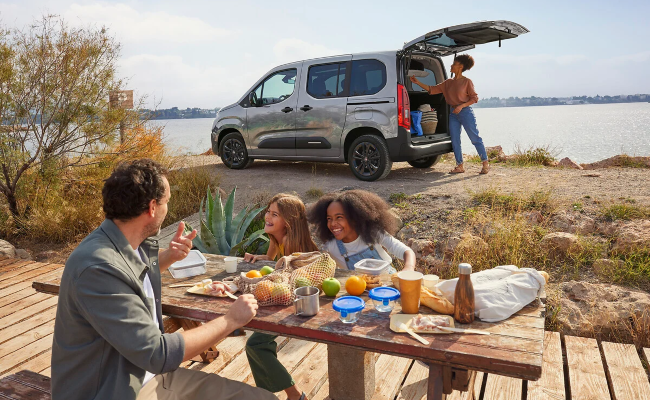 Family eating at a picnic table in front of a parked Citroen Berlingo with the boot open